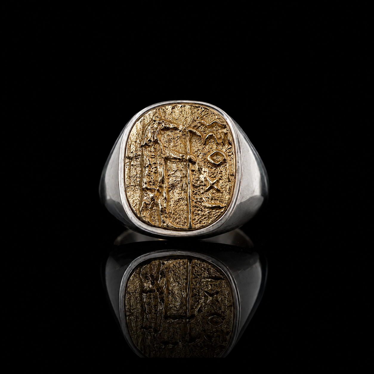 A silver signet ring with a large oval Anubis gold-toned face featuring an engraved ancient script, displayed on a reflective black surface.
