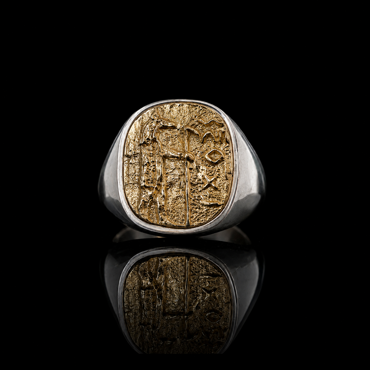 A silver signet ring with a large oval Anubis gold-toned face featuring an engraved ancient script, displayed on a reflective black surface.