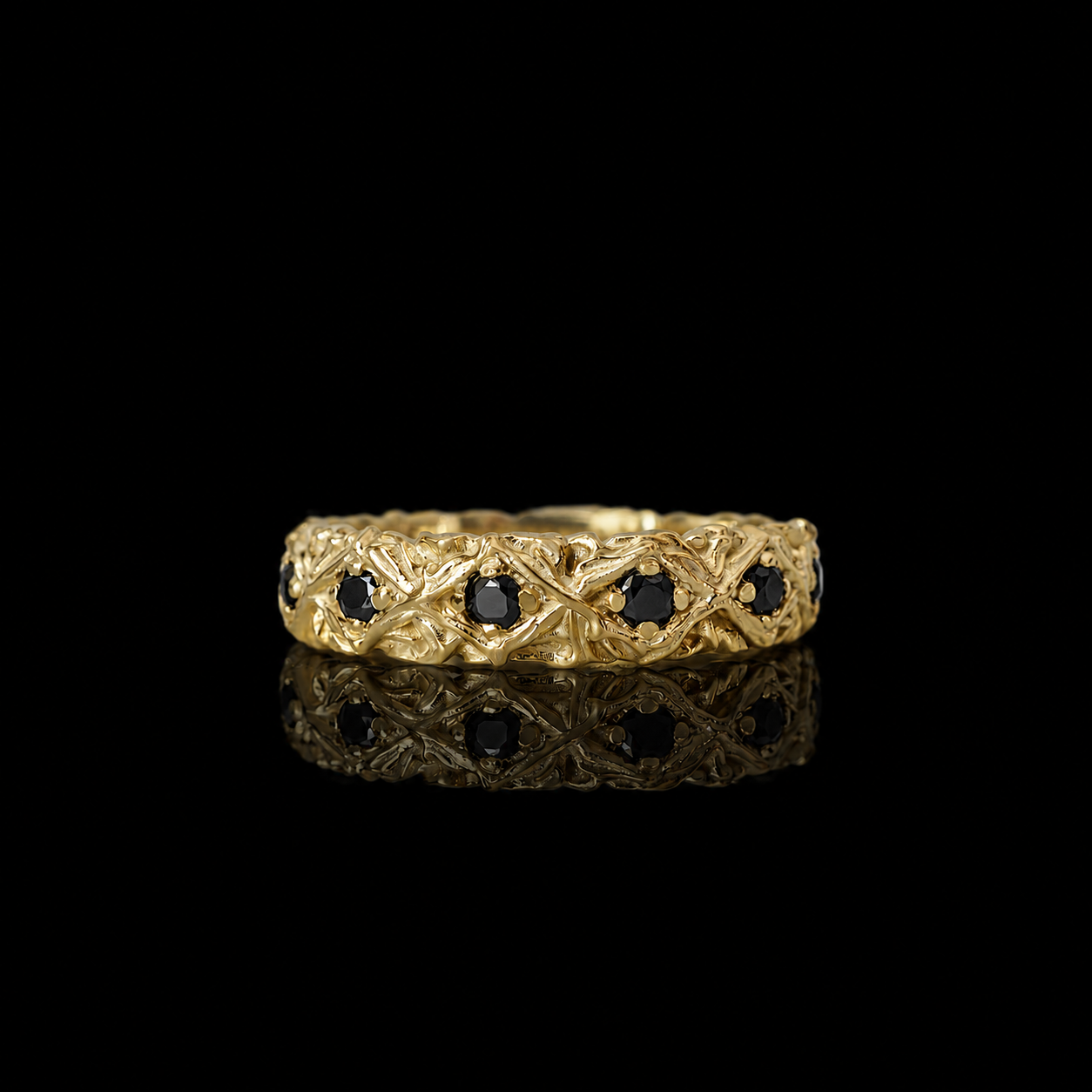 A yellow gold eternity ring featuring a detailed geometric lattice pattern and small round black diamonds set along the band, displayed against a solid gold setting.