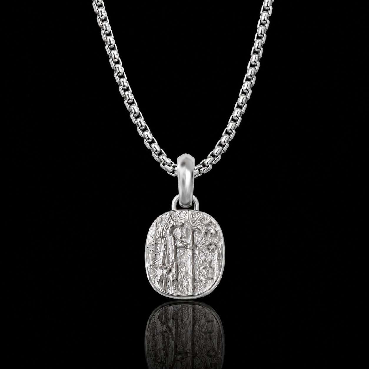 A silver chain necklace with a round, textured pendant featuring an engraved Anubis god, displayed against a solid black background with a soft reflection below.