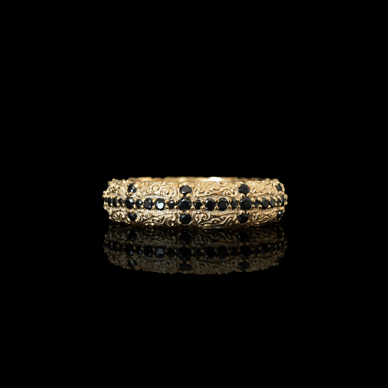 A gold filigree band ring with rows of small dark black diamonds, photographed on a black reflective surface against a black background.