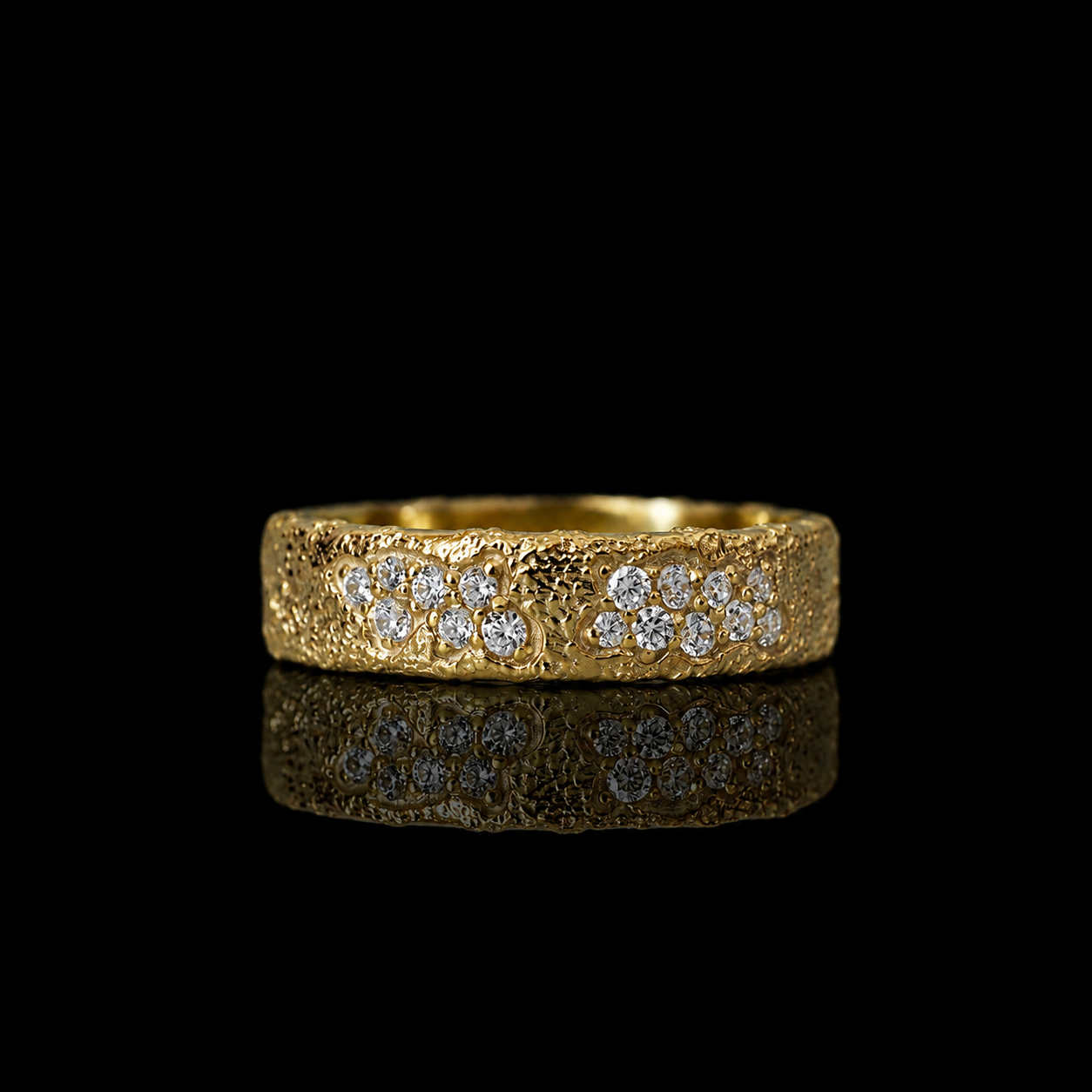 A textured yellow gold ring featuring two rows of round-cut diamonds, displayed on a reflective black surface against a solid black background.