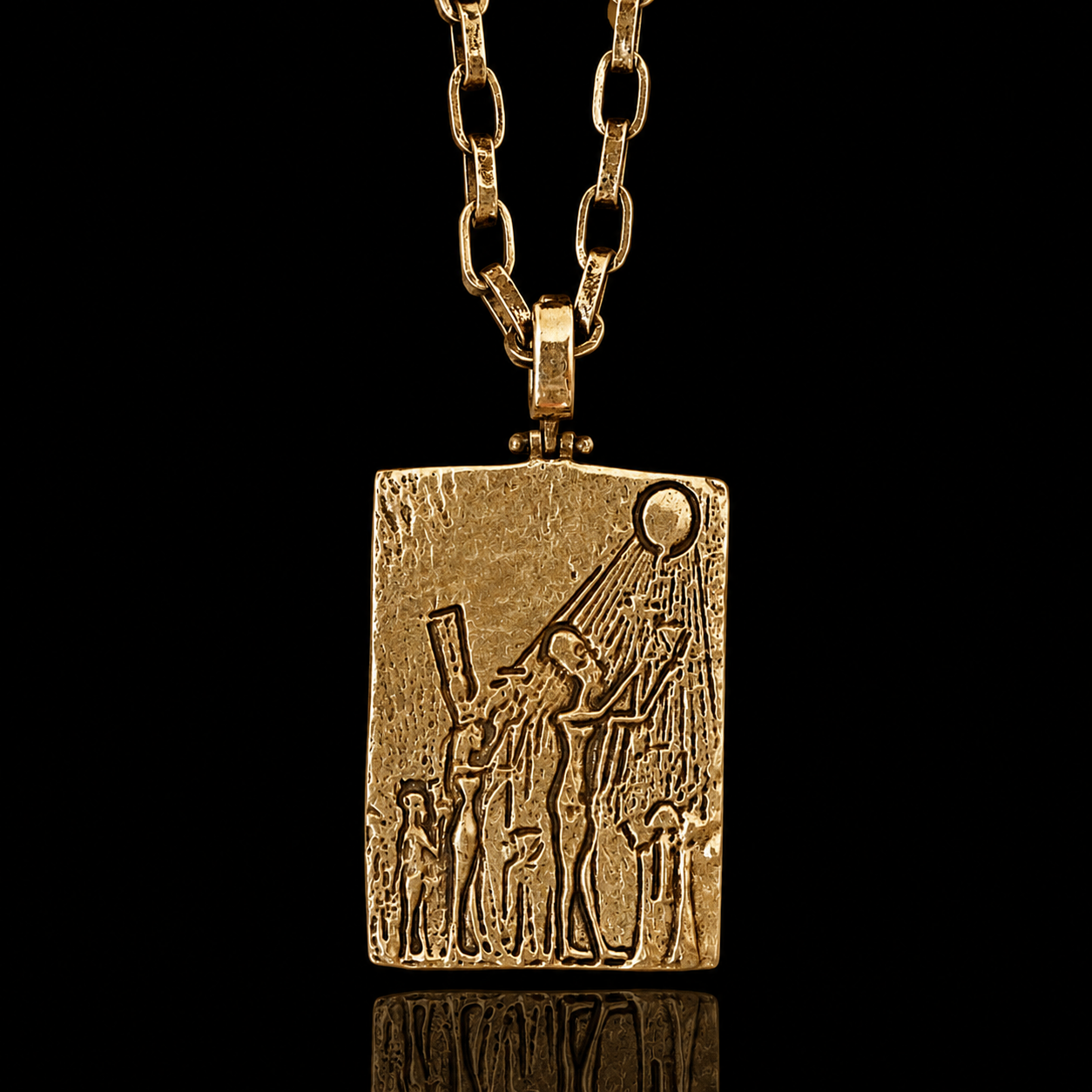 A gold pendant necklace featuring an embossed rectangular plaque with a stylized figure and sun motif, suspended from a gold chain against a solid black background.