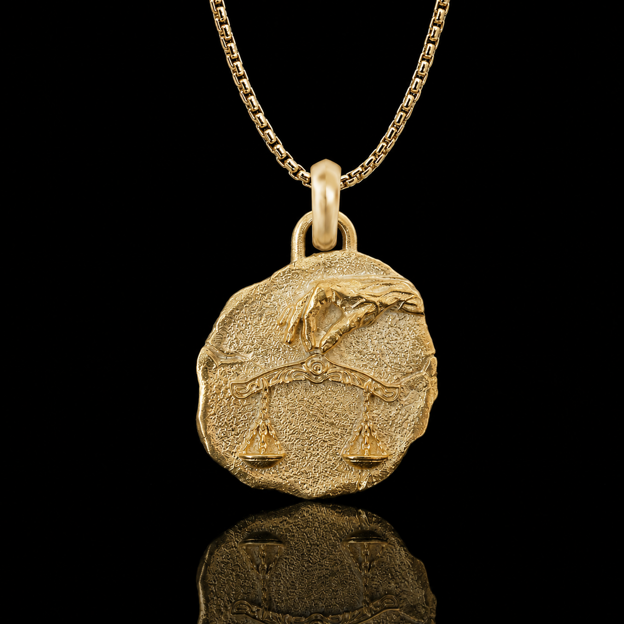 A textured gold pendant necklace featuring the Libra zodiac symbol, suspended from a gold chain against a solid black background with a clear reflection below.