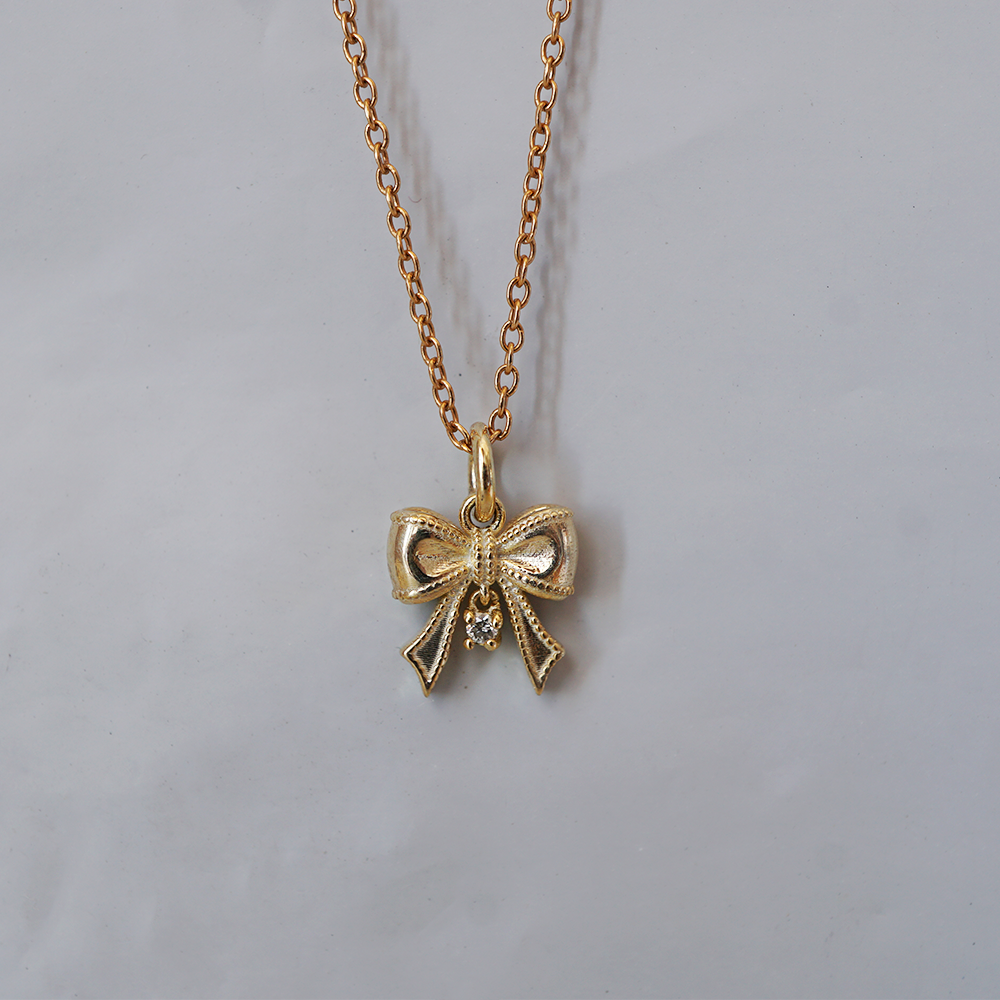 The Bow solid gold ribbon charm with a dangling natural diamond