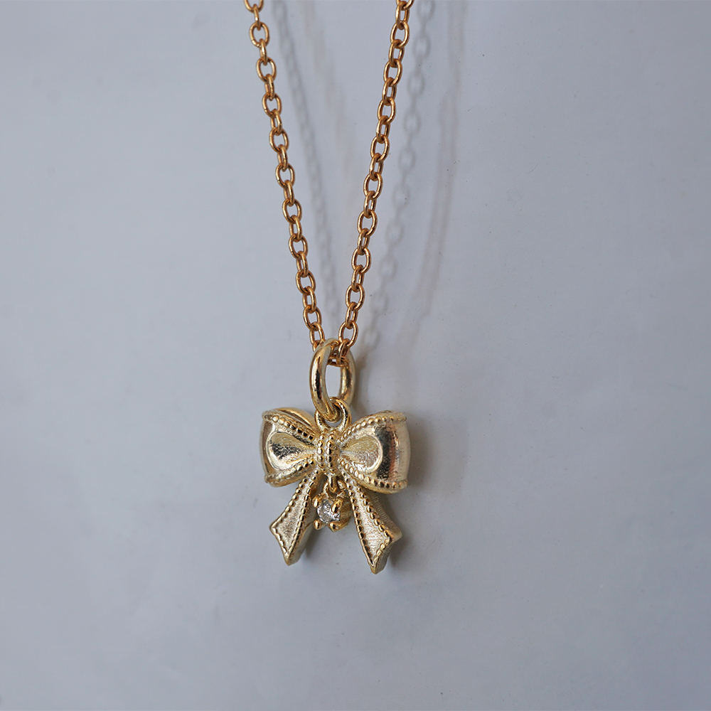 The Bow solid gold ribbon charm with a dangling natural diamond, alternate view