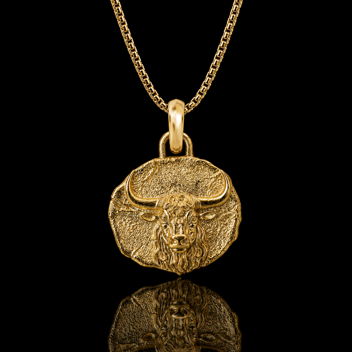A gold bull pendant necklace on a matching chain, displayed against a solid black background with a clear reflection below.